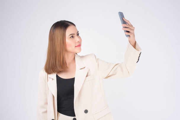 Porträt einer jungen schönen Frau im Anzug mit Smartphone vor weißem Hintergrund - Foto, Bild