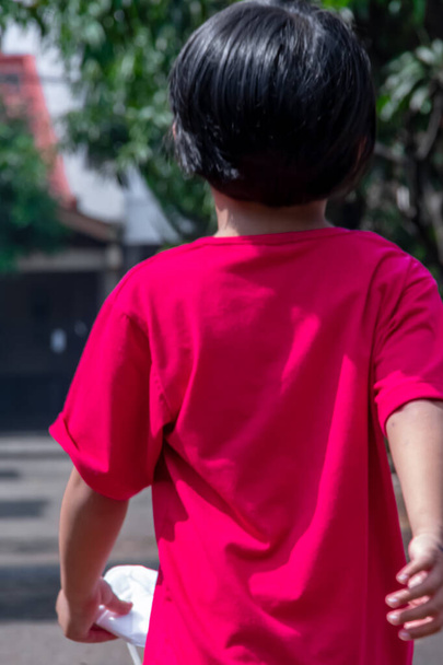 Un jeune garçon courageux porte un t-shirt rouge marche avec confiance dans la rue va jouer - Photo, image