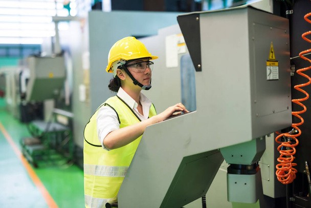 Waist up woman engineer with hardhat and protection glasses command monitor screen and console to control transistor microchip machines in factory workshop. Manufacturing industry with technology. - Photo, Image