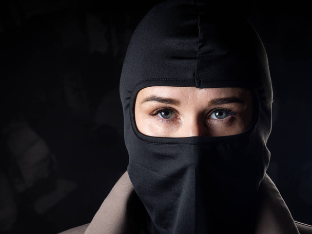 Portrait of a girl in a black balaclava and beige coat. Shot in the studio on a dark background. - Photo, Image
