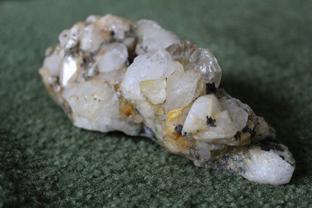 close-up of natural unprocessed rock crystal on a green background / photo of a beautiful unprocessed stone.large natural rhinestone. white, transparent color. inclusions of yellow and black. - Foto, Imagem