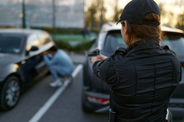Policewoman aiming gun at car thief backview - Фото, изображение