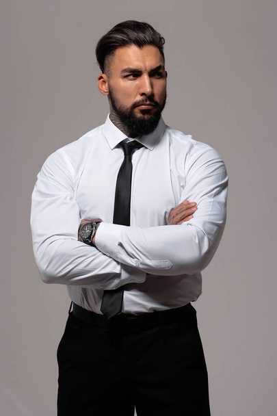 Parrakas latino kaveri tumma liivi ja valkoinen paita solmio katselee kameraa kädet taskussa studiossa - Valokuva, kuva