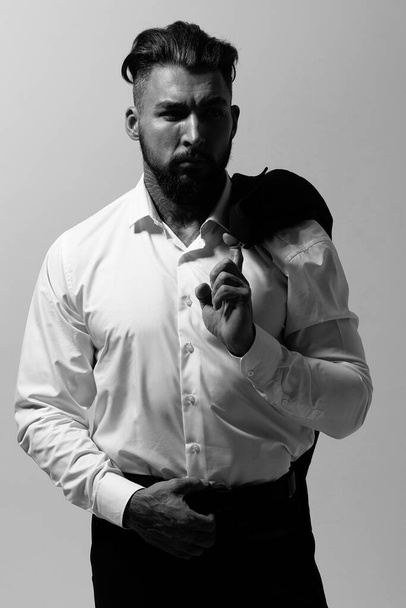 Szakállas spanyol fickó sötét mellényben és fehér ingben, nyakkendővel a kamerát nézve, kezekkel a zsebében a stúdióban. - Fotó, kép