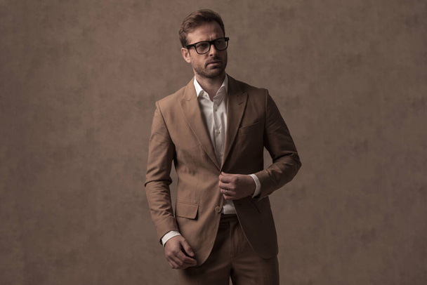 sexy businessman closing his jacket, wearing eyeglasses and looking away in a fashion pose - Photo, image