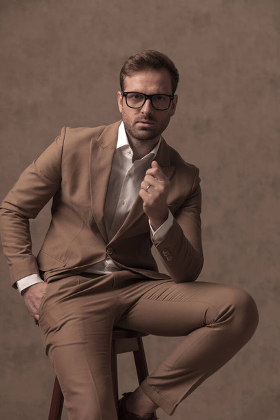 seated businessman wearing eyeglasses, holding one hand in pocket in a fashion pose - Foto, afbeelding