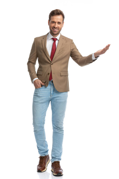 young businessman greeting someone with a smile on his face and one hand in pocket against white background - Foto, Imagen