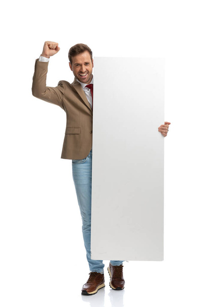 sexy businessman celebrating success and holding a blank board against white studio background - Foto, imagen