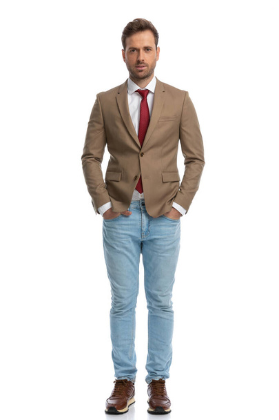 handsome businessman holding his hands in pockets and posing against white studio background - Valokuva, kuva