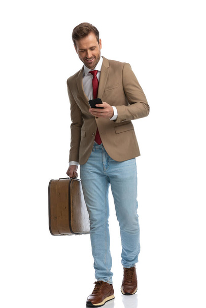handsome businessman writing a message on his phone while walking and holding a briefcase - Foto, Imagem