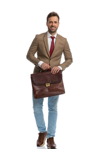 young handsome businessman walking towards the camera with a briefcase and a smile on his face - Fotografie, Obrázek