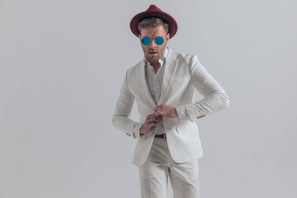 sexy businessman opening his jacket, wearing sunglasses, a burgundy hat in a fashion pose - Foto, Imagen