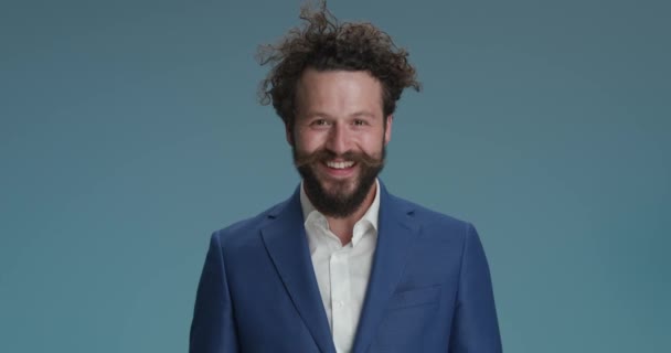 video portrait of bearded young man being enthusiastic, clapping, laughing and having fun, pointing fingers, holding fists up and celebrating on blue background in studio - Záběry, video