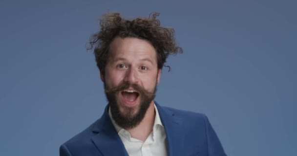 dancing man with curly hair on blue background having a good time, moving in a dynamic, energy manner, shaking and gesturing in studio - Video