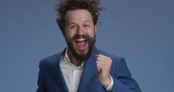 happy young man with beard and moustache dancing, moving and having a good time, holding hands up and laughing in front of blue background - Felvétel, videó