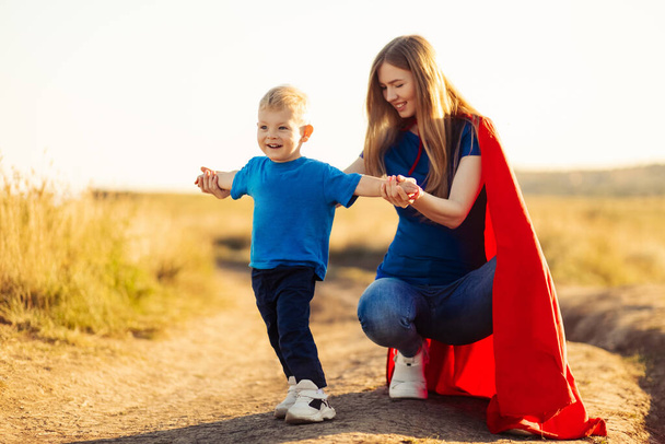 Mother and her child play together outdoors. Mom and son in superhero costumes. Mom and baby have fun, smile and hug. Family vacation and togetherness. Concept of Mother's Day, family - 写真・画像