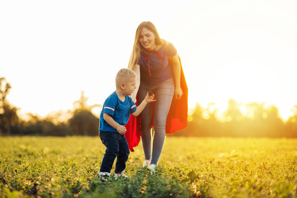 family spending time together, mom and son plant a tree in the park, mom and son in superhero costumes, Side view of family plant a tree in a meadow on a sunny spring day. save the world concept - Фото, изображение