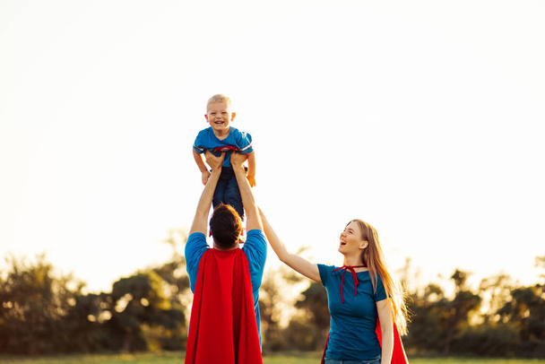 concept of european superfamily, outdoors, loving father holds on the neck, superhero family run at sunset in nature, dad raises his son to the sky - Photo, image