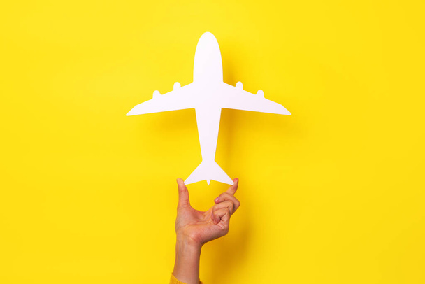 mano che tiene il simbolo dell'aeroplano su sfondo giallo, concetto di viaggio - Foto, immagini