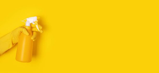 mano en un guante sosteniendo una botella de spray sobre fondo amarillo, concepto de limpieza, diseño panorámico - Foto, imagen