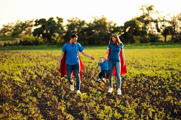 concept of european superfamily, outdoors, loving father holds on the neck, superhero family run at sunset in nature, father, mom and son are holding hands - Photo, image