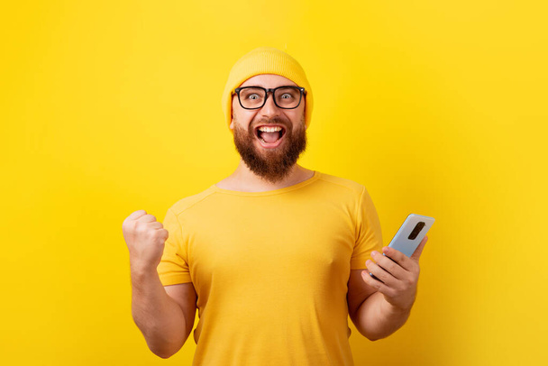 uomo in possesso di telefono su sfondo giallo, concetto vincitore - Foto, immagini