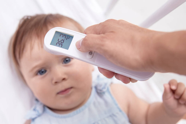 Mother checks baby's  temperature with modern electronic termomether at baby's forehead - Foto, Bild