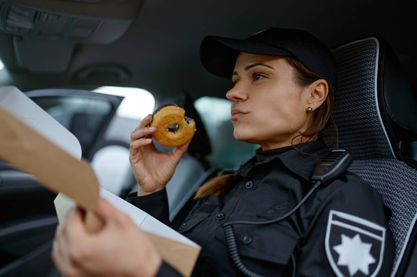 Γυναίκα αστυνομικός τρώει ντόνατ στο αυτοκίνητο - Φωτογραφία, εικόνα