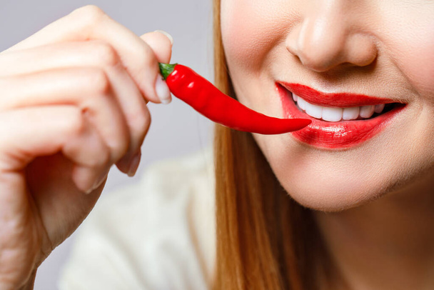 Woman with chili red pepper isolated en blue background. Sexy female lips. Hot seductive girl. - Фото, изображение