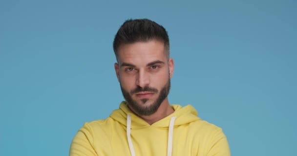 young casual man smiling at the camera and wearing a yellow hoodie against blue background - Footage, Video