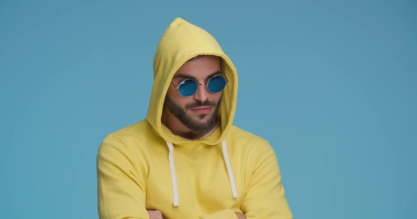 young casual man with crossed arms is removing his hood and sunglasses and making big eyes, covering his mouth and laughing - Footage, Video