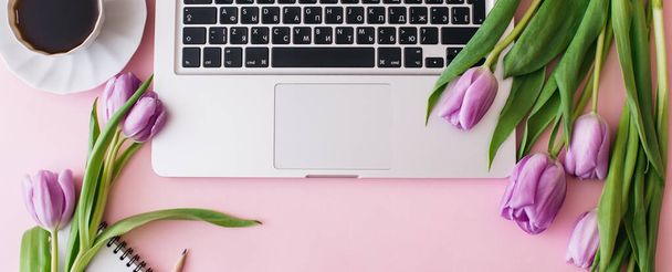 Banner made Workspace with laptop, tulip flowers, cup of coffee on pink background. Home office desk. Flat lay, top view, copy space for text. Spring concept. - 写真・画像