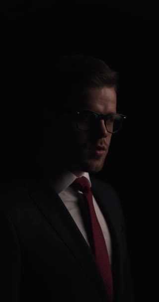 unshaved businessman wearing eyeglasses, looking to side and touching palms, being dramatic and making a video in a mysterious background in studio - Záběry, video