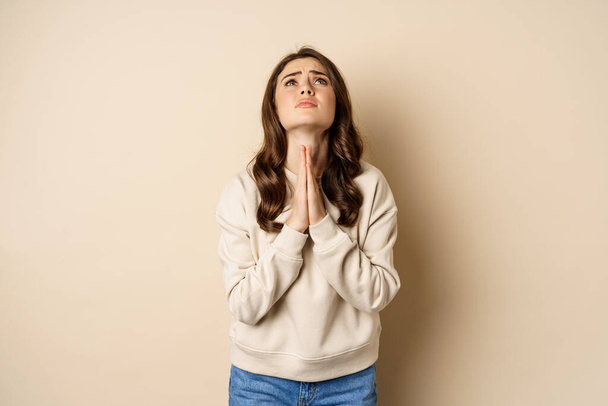 Woman begging and pleading god, supplicating, say please, standing desperate over beige background - Photo, image