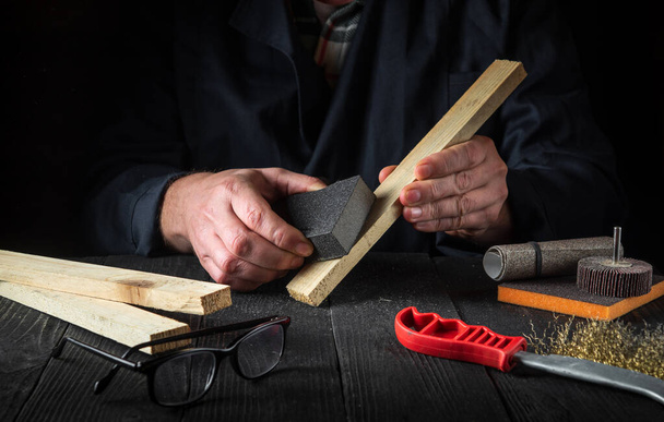 Un artisan professionnel nettoie la planche de bois avec un outil abrasif. Les mains du constructeur se rapprochent. Rénovation ou idée de construction. - Photo, image