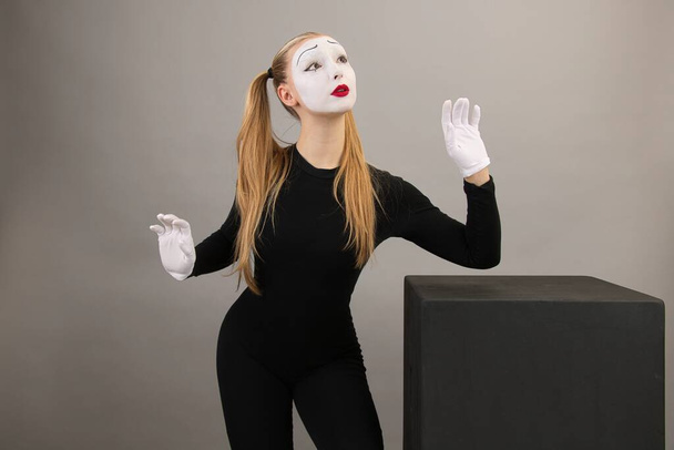 Circus girl, mime near the black cube. In emotion of admiration, on a gray background. - Foto, Imagen