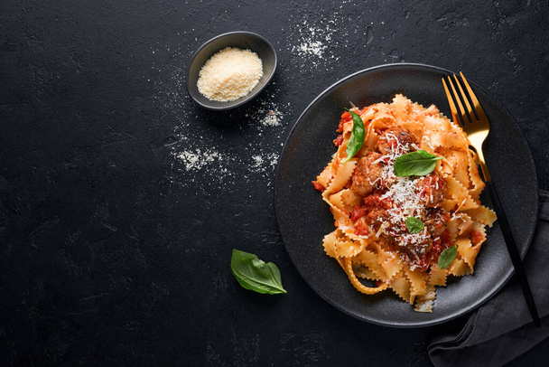 Tagliatelle pasta with meatballs in tomato sauce, basil and parmesan cheese on black stone or concrete background. Traditional Italian dish and cuisine. Top view with copy space. - Fotoğraf, Görsel