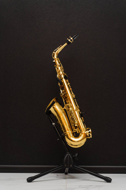 Sax μουσικό όργανο για να παίξετε τζαζ. Μουσικό όργανο σαξοφώνου σε στάση σε μαύρο φόντο - Φωτογραφία, εικόνα