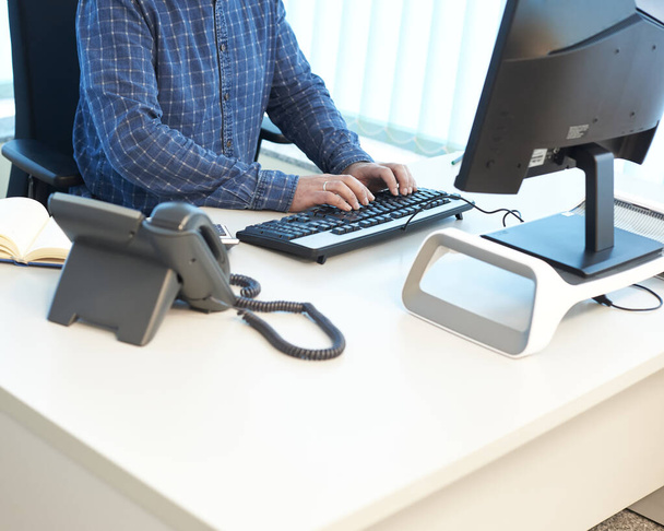 Mann tippt auf einem Computer an einem Schreibtisch im Büro, Frontansicht und von oben, der Mann ist unkenntlich und es gibt freien Platz für Text - Foto, Bild