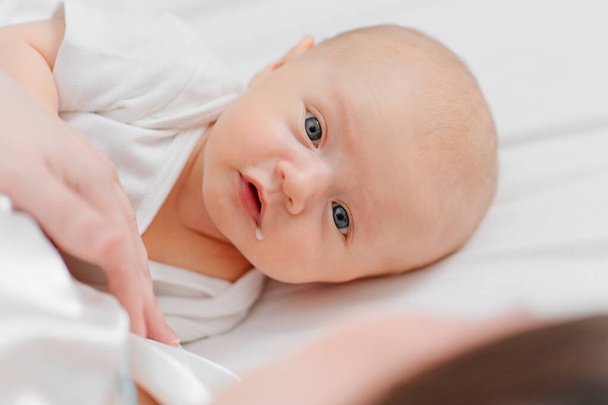 un lindo bebé con una gota de leche en la esquina de la boca en la cama cerca de la madre. - Foto, imagen