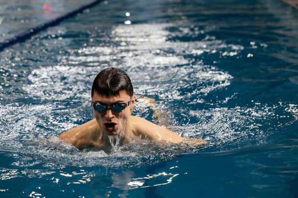 Caucasian athlete-swimmer crawls in the blue water. Portrait of a young male triathlete swimming in swimming goggles. Triathlon training concepts for triathletes - Foto, Bild