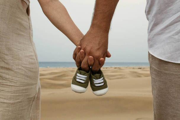 Parents holding a baby's shoes. Brown man and white woman - Photo, Image