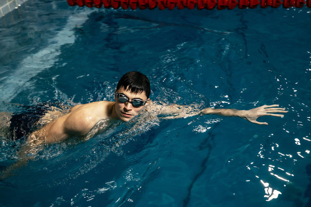 Καυκάσιος αθλητής-κολυμβητής σέρνεται στα γαλάζια νερά. Πορτραίτο νεαρού τριαθλητή που κολυμπάει με γυαλιά κολύμβησης. Εκπαιδευτικές έννοιες τριάθλου για τριαθλητές - Φωτογραφία, εικόνα