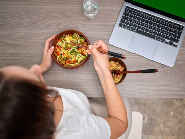 コンピューターの前で箸で食べる女性の上からの眺め - 写真・画像