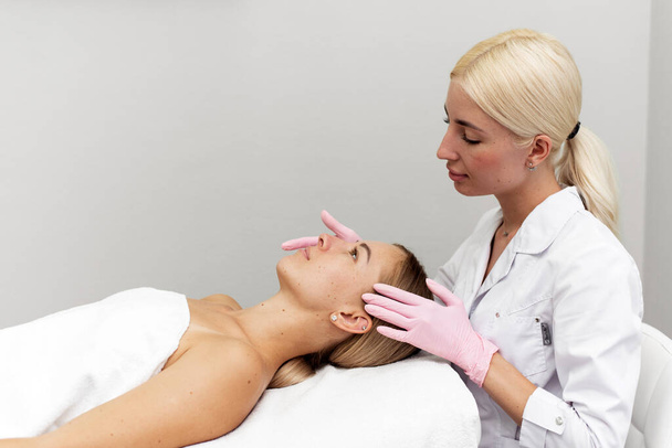 Young beautician or dermatologist doing manual facial cleansing for a woman in a beauty salon. Spa facial massage. Beautiful woman receiving facial massage in a beauty salon. The beautician makes - Valokuva, kuva