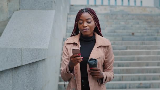 Frustrated African American businesswoman walking stairs with disposable cup of coffee and telephone. Sad young woman receiving unpleasant cancellation message, annoyed worried by bad news, problems - Video