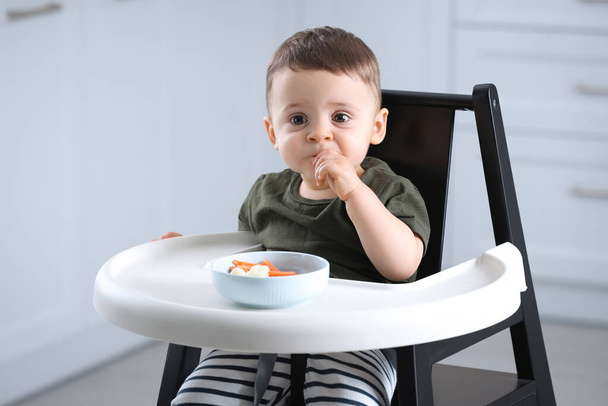 Cute little baby eating healthy food in high chair at home - Photo, Image