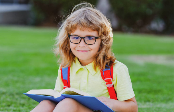 Back to school. Funny little boy in glasses near school. Child from elementary school with book and bag. Education. Child with a book. - Photo, Image