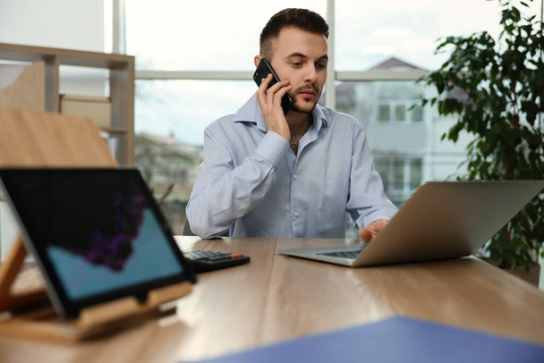 Forex trader talking on phone while working with laptop in office - Foto, Imagem
