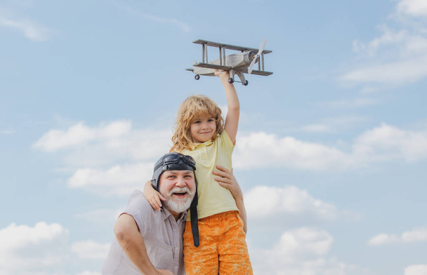 Child boy and grandfather with toy jetpack plane against sky. Child pilot aviator with plane dreams of traveling. - Foto, afbeelding